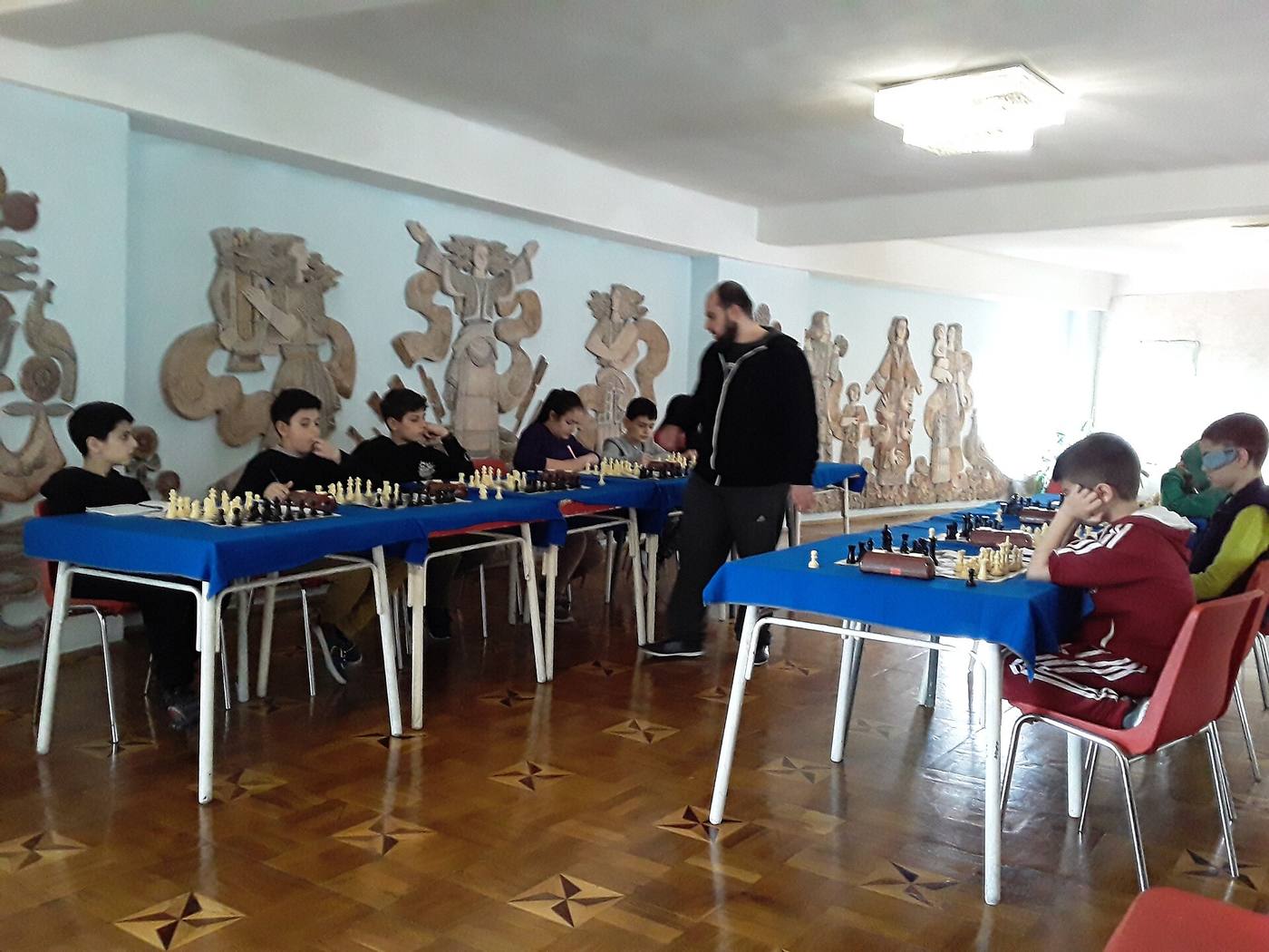 Гроссмейстер ходит вдоль длинных столов и играет одновременно с несколькими детьми