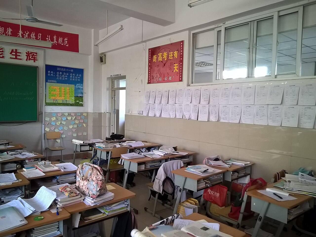 Класс старшей школы: парты завалены стопками учебников, на стене лозунги