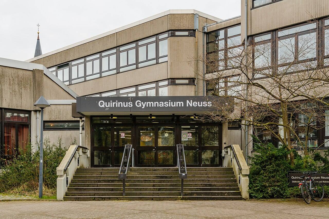 Вход в бетонное здание школы с вывеской Quirinus Gymnasium Neuss